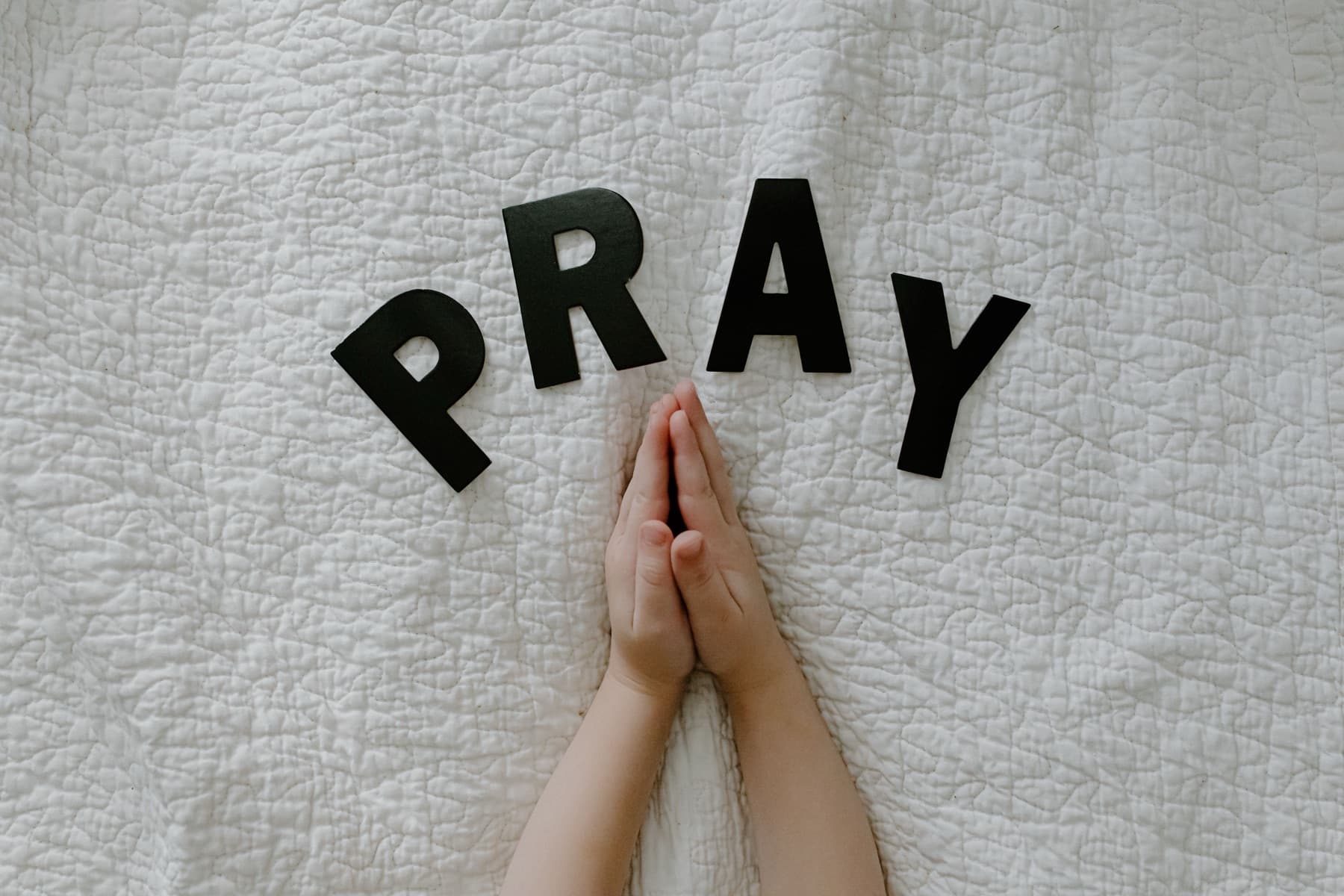 A child's hands folded in prayer beside paper letters spelling PRAY